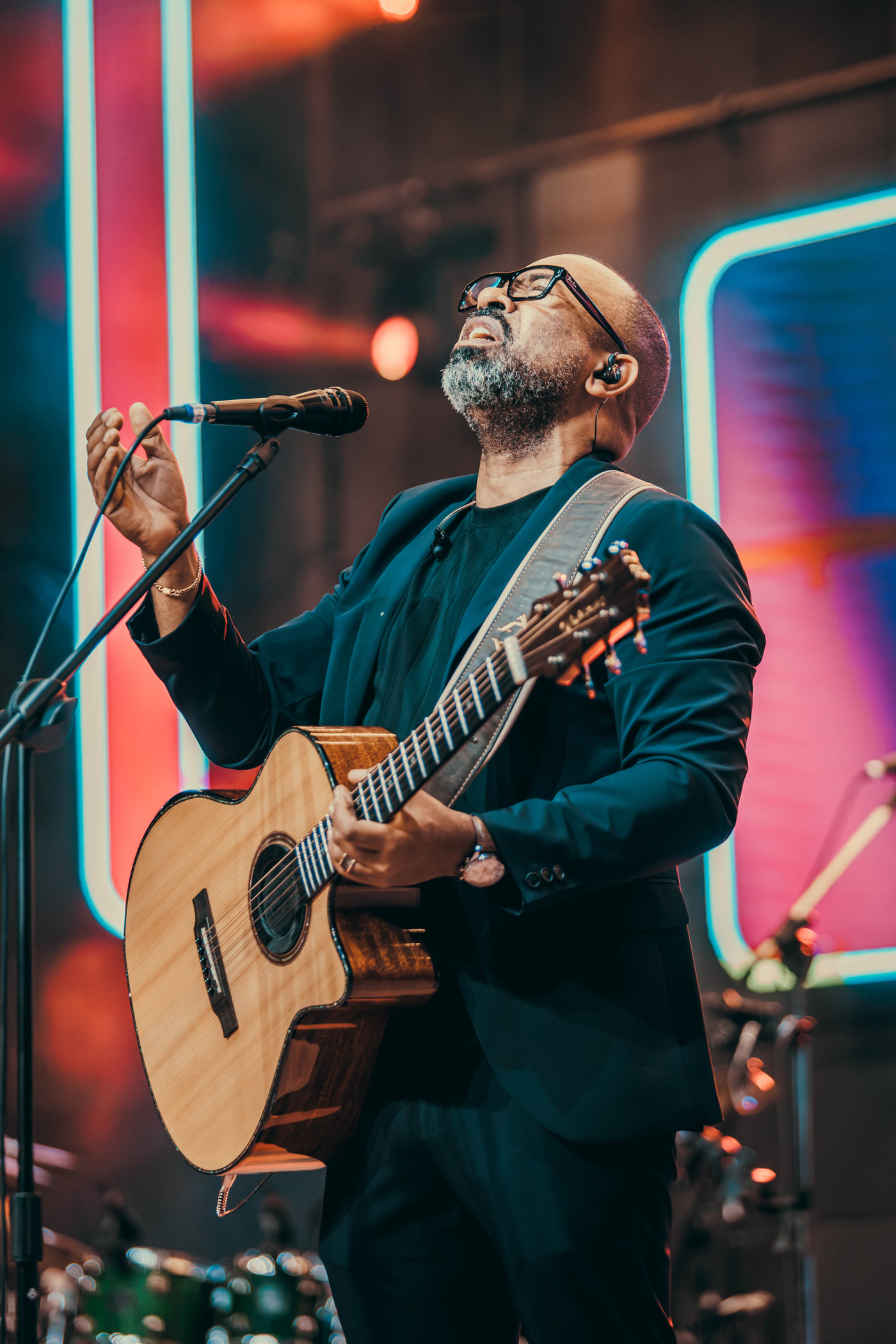Luiz Arcanjo cantando com violão sob luzes coloridas
